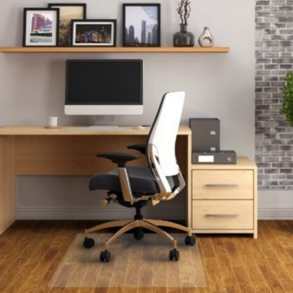 A modern home office setup with a sleek desk, ergonomic black and tan office chair, and a PVC floor mat. The room features wooden flooring, a gray brick wall, and a shelf with decorative items and framed pictures, creating a stylish and functional workspace.