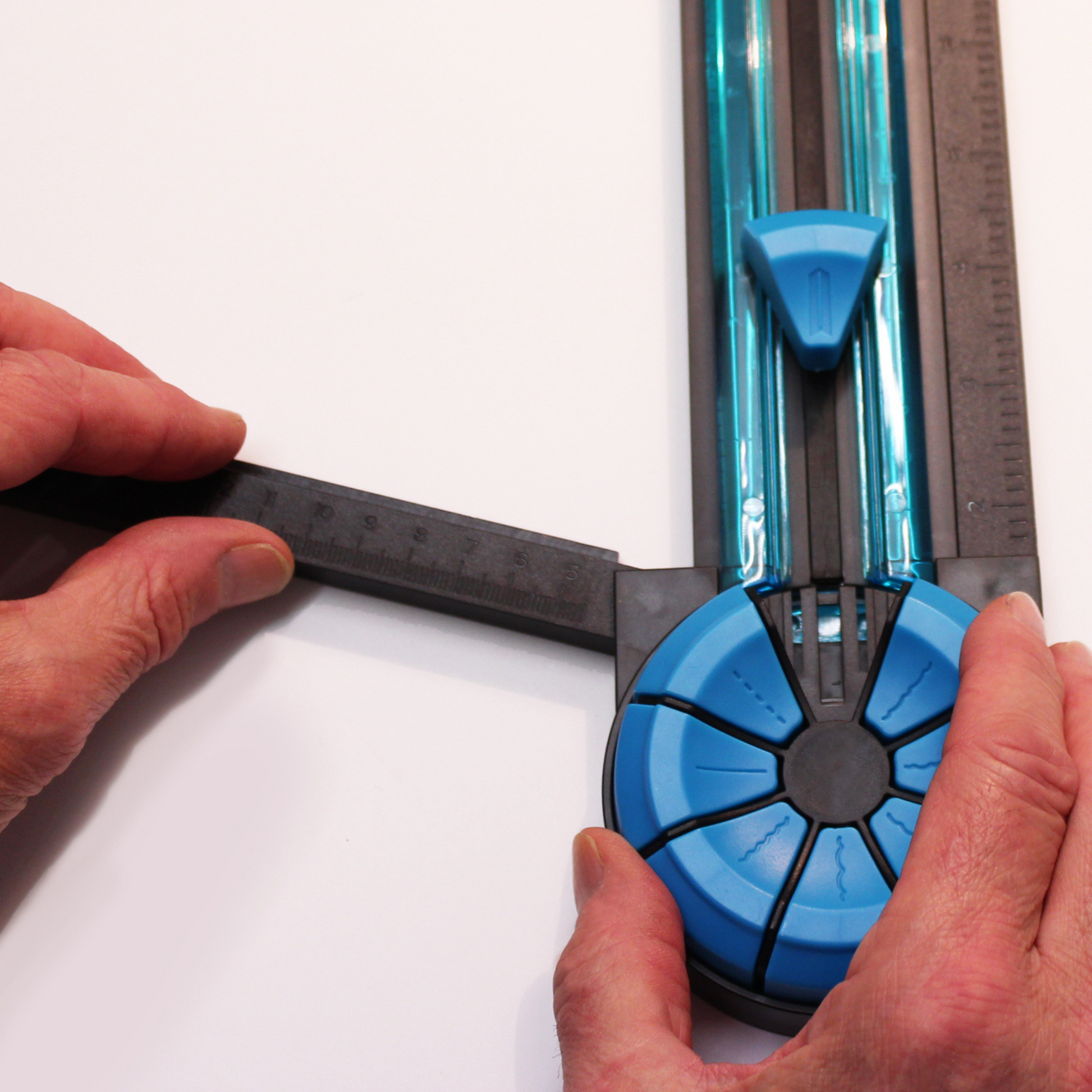 Hands precisely adjusting the blue dial of an A4 Dial-A-Blade Creative Trimmer, with a focus on the measurement ruler and cutting track, demonstrating the trimmer's functionality for detailed paper cutting tasks.