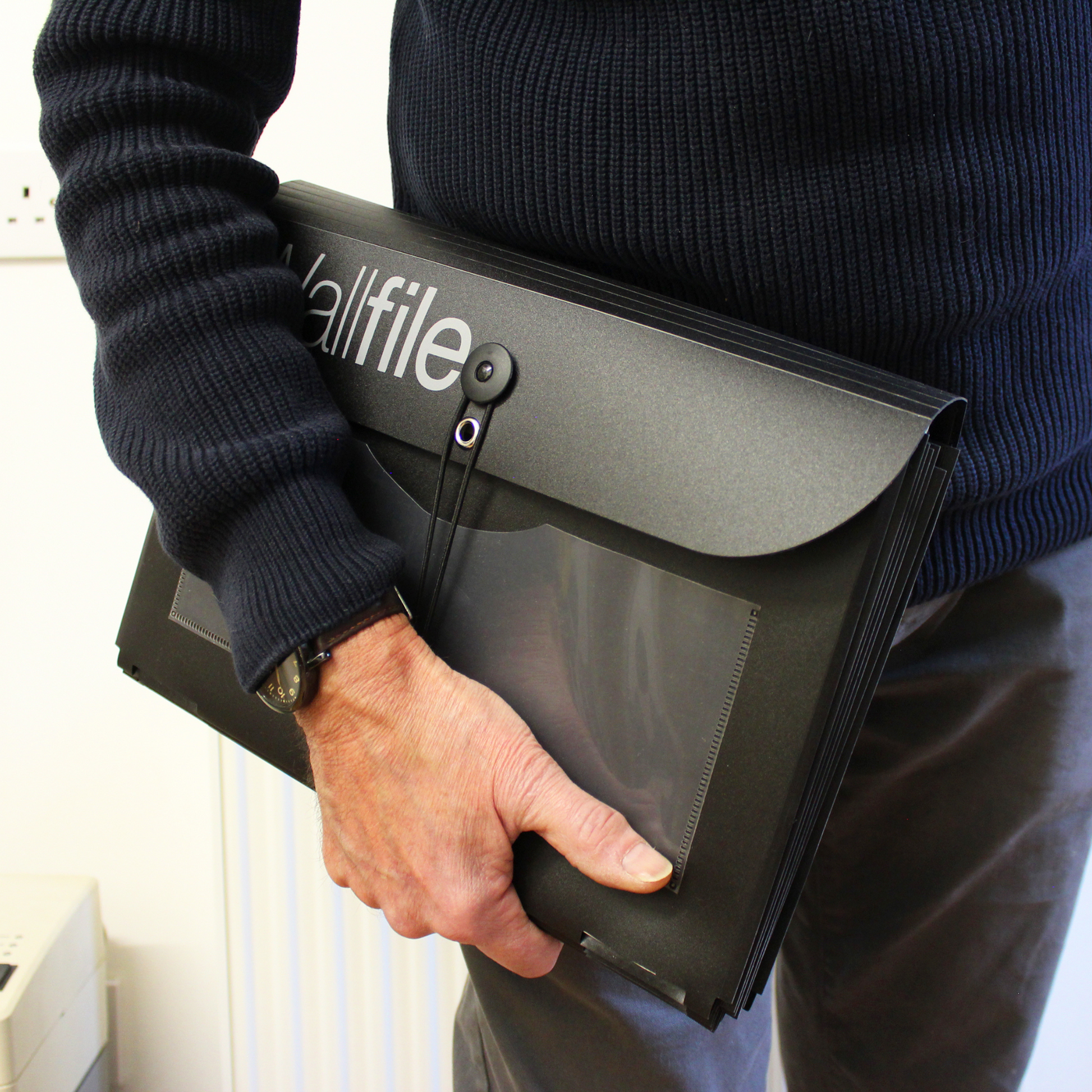 Person holding a black Wallfile organizer under their arm, illustrating the portability and lightweight design of the product for easy transport and setup.