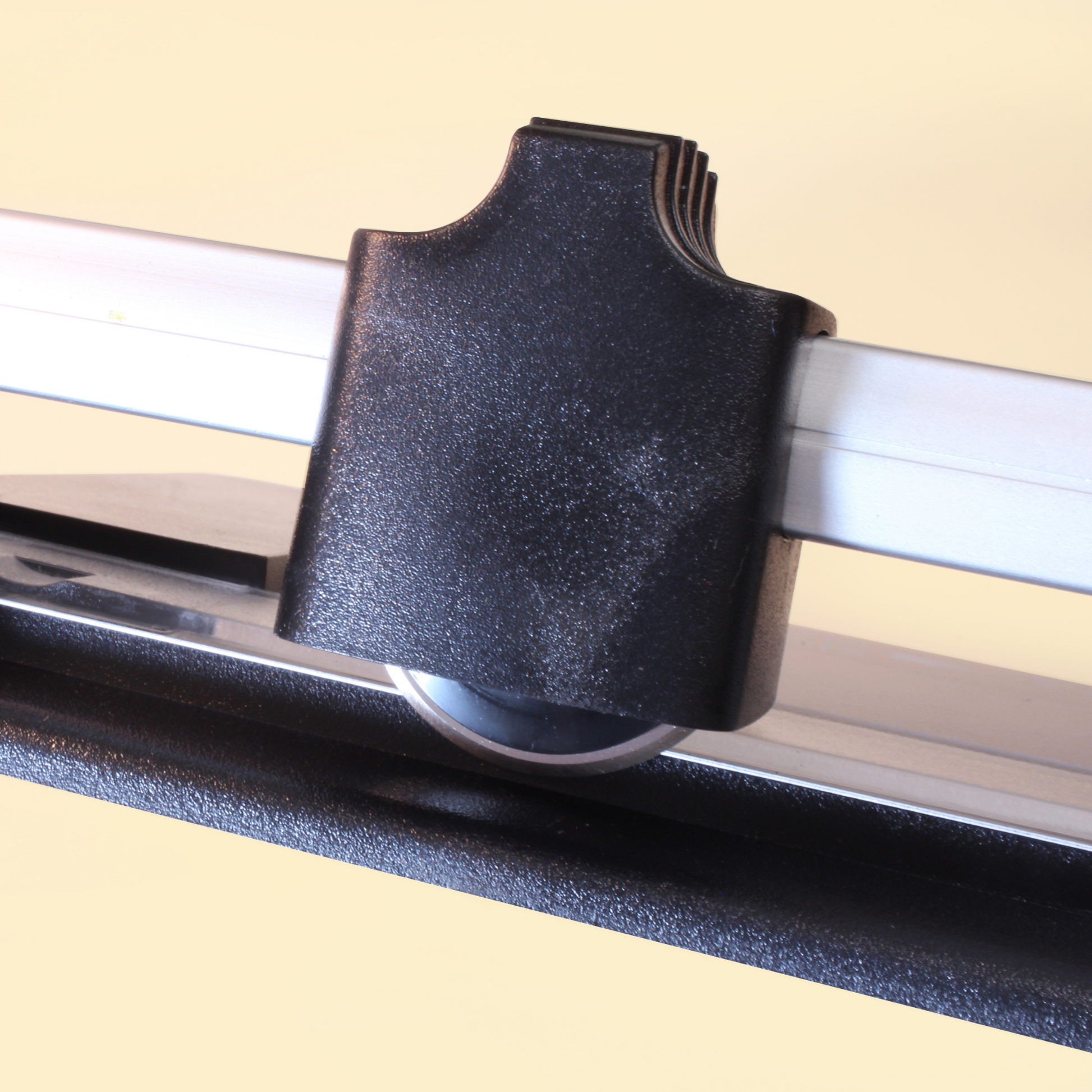 Close-up of the black cutting head on an A4 rotary paper trimmer, showing the ridged edge for a firm grip and the circular blade beneath, set against the metal guide bar for precision in paper trimming.
