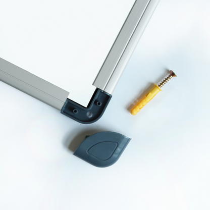 Close-up of a whiteboard corner with a silver aluminum frame and black corner protector, next to a yellow wall anchor and screw for mounting.