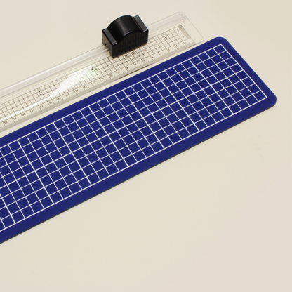 An A4 size blue cutting mat paired with a transparent cutting ruler with a black rotary blade cartridge, positioned on a light background.
