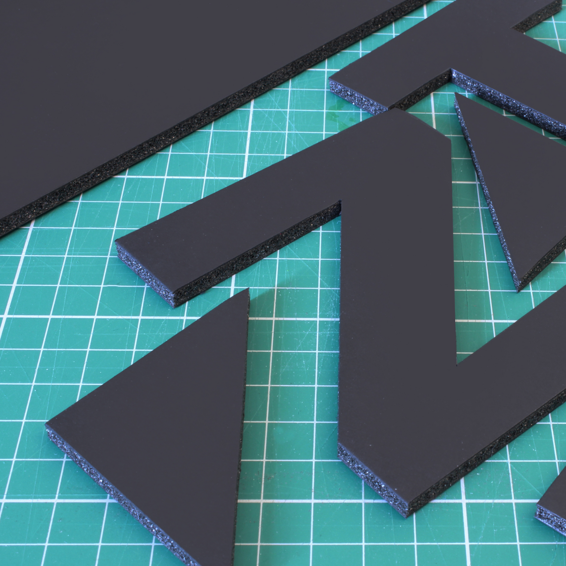 Creative display of cut-out black 5mm foam board pieces, letters Z and T cut from a sheet of foamboard, on top of a green cutting mat, showing the boards many applications and ease of use.