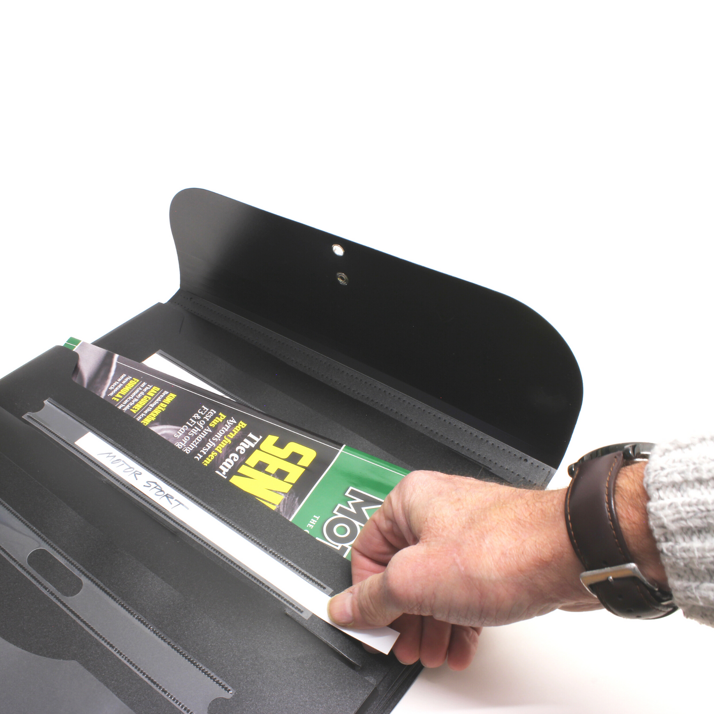 A person's hand placing magazines into a black wall-mounted Wallfile organizer, illustrating its ease of use and practical design for document storage.