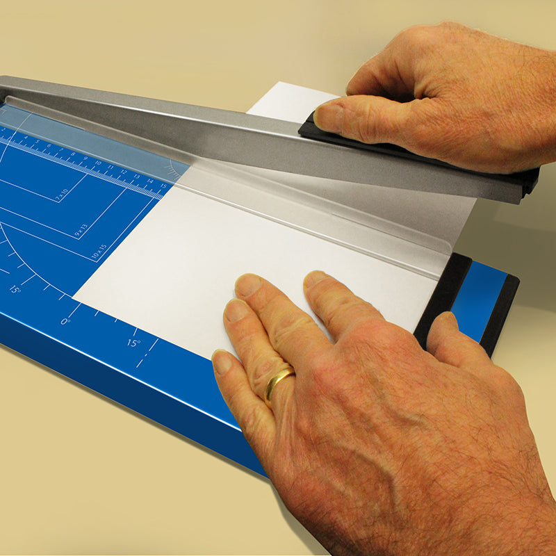 Close-up of a person's hands using an A4 paper guillotine cutter on a metal base, precisely aligning the paper for cutting.