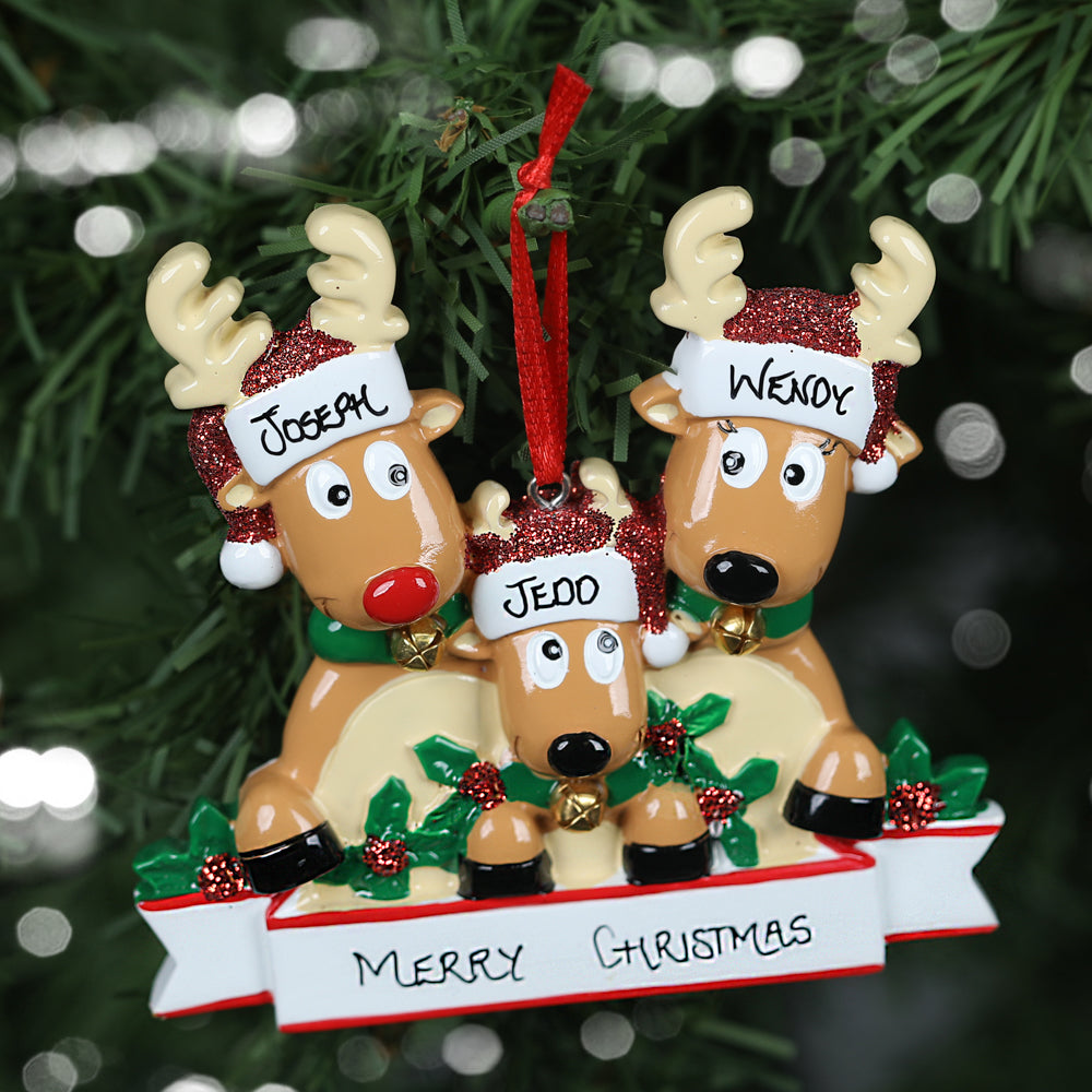 A personalized Christmas ornament depicting a reindeer family of three with the names 'Joseph', 'Paul' and 'Penny' on their glittery Santa hats, showing the personalisable capabilities of the ornament. The ornament is hanging on a festive tree. Below them, a banner reads 'Merry Christmas,' set against a backdrop of twinkling lights.