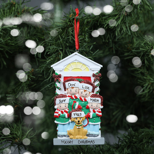 A personalized Christmas tree ornament depicting a family of four with their dog in front of a house, labeled 'Don', 'Lisa', 'Jeff', 'Maria', and 'Fred' on the dog's Santa hat, showing the personalisable capabilities of the ornament. The festive decoration includes a handwritten 'Merry Christmas' banner and is set against a background of a Christmas tree with blurred lights.