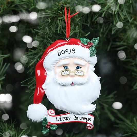 A personalized Christmas decoration featuring a jolly Santa Claus face with the name 'Boris' on his hat, showing the personalisable capabilities of the ornament. The ornament is complete with a 'Merry Christmas' banner and hangs from a red ribbon against the festive backdrop of a Christmas tree with twinkling light bokeh.