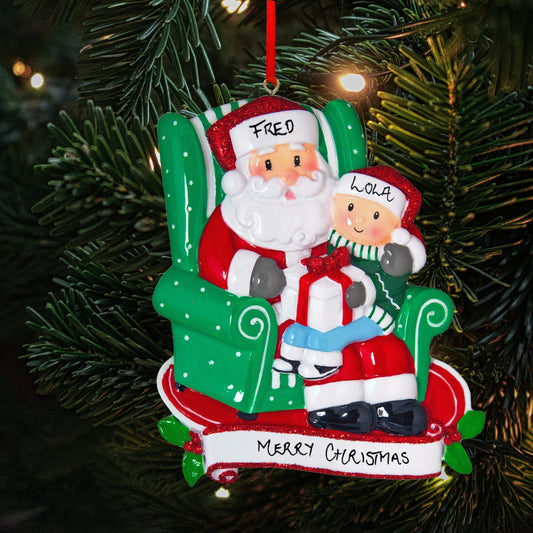 Personalized Christmas tree ornament featuring Santa Claus and a child with the names 'Fred' and 'Lola' written on their hats, set against a festive backdrop of green pine needles, with 'Merry Christmas' inscribed below.