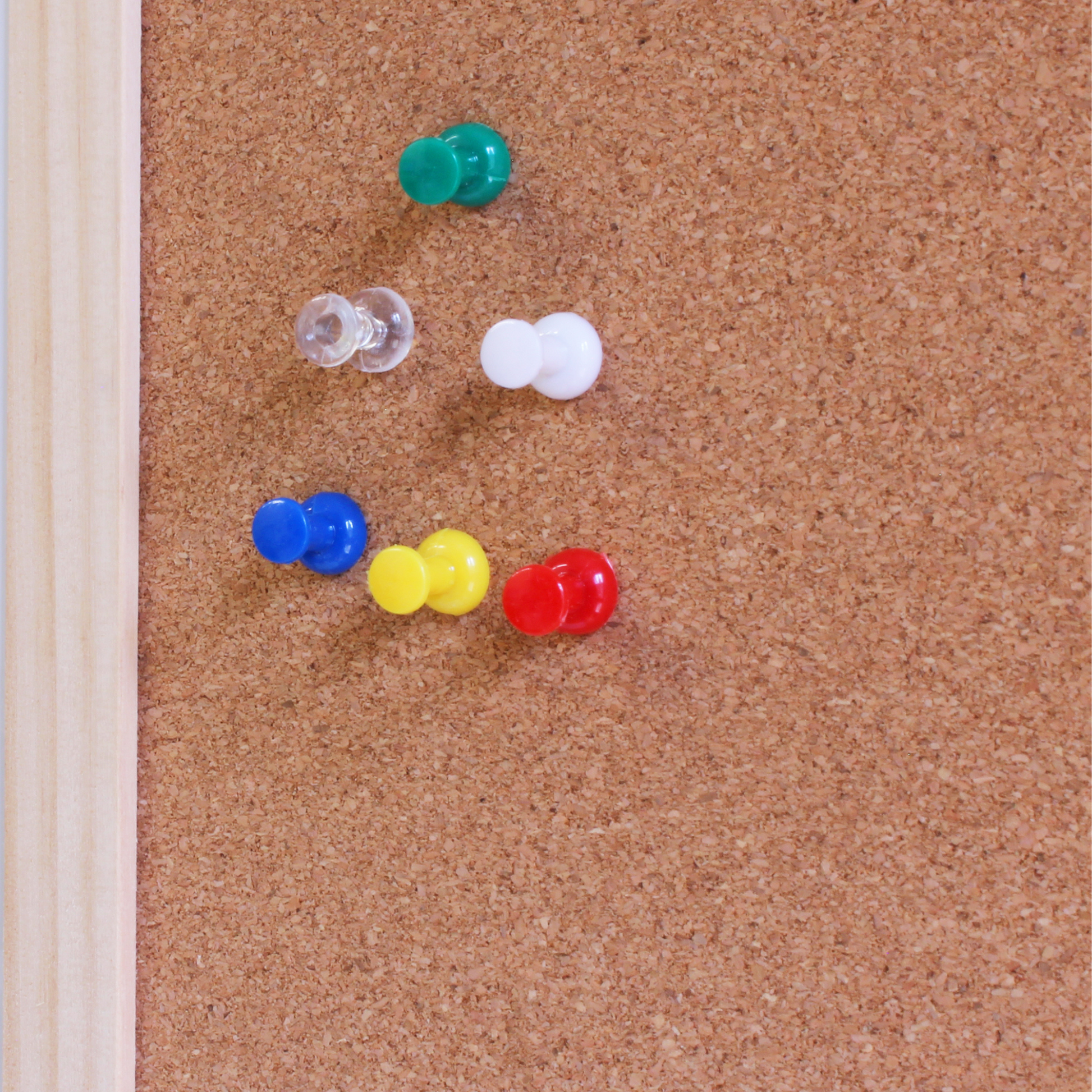 Corkboard with colorful pushpins: red, blue, yellow, green, white, and clear.